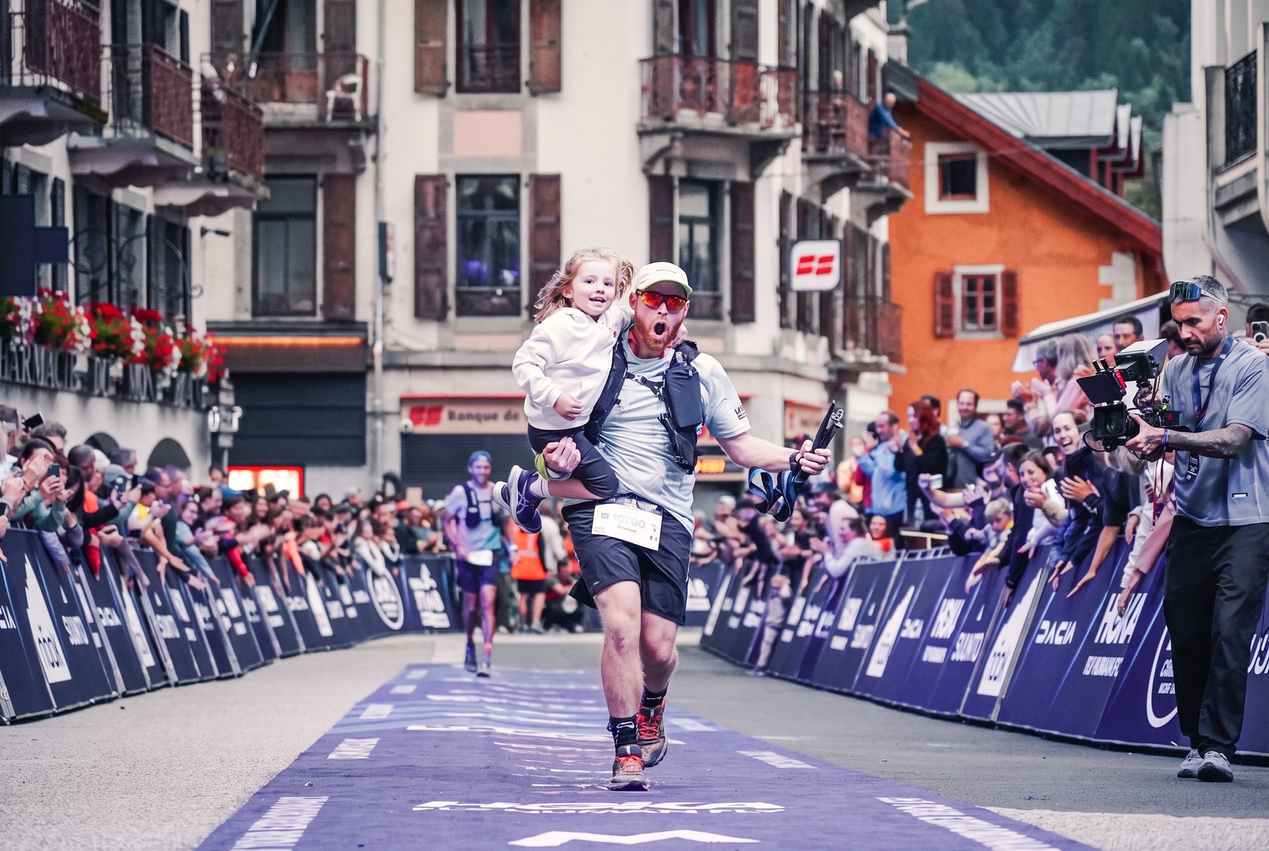 Coureur franchissant une arrivée de trail avec sa fille dans les bras